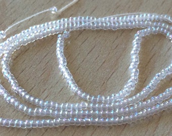 May include: A strand of iridescent white seed beads, strung on a white thread. The beads are small and round, and they have a subtle shimmer.