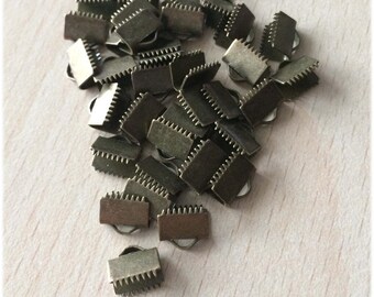 May include: A pile of 8 mm antique brass metal clasps. The clasps are rectangular with a serrated edge and a small hole in the center.