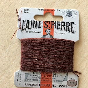 Peut inclure: Une bobine de fil à broder marron avec l'étiquette "LAINE STPIERRE" et le texte "LES LAINES MARQUE STPIERRE sont recommandées pour tous les travaux de Dames REPRISER BRODER FESTONNER coloris 210".