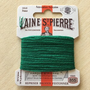 May include: A spool of green embroidery floss labeled "Laine St. Pierre" with the text "Fabrication française" and "Ets Toulemonde Successeurs". The label also includes the text "50% laine 50% polyamide" and "coloris 855".