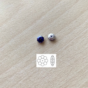 May include: Two flower-shaped beads, one deep blue and one silver, are displayed on a light wood surface. A small diagram of the bead's design is also present, showing a top and side view of the flower shape.