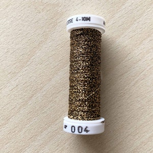 May include: A spool of gold metallic thread with a white label that reads "004" and "ESSE 4-10M".