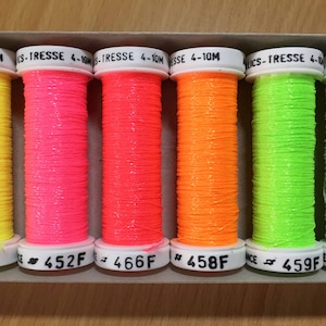 May include: Six spools of neon-coloured thread with glitter. The spools are labelled with numbers and the letter "F".