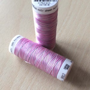 Peut inclure: Deux bobines de fil rose et argent avec une étiquette blanche qui indique "100% Polyester" et "9912 JAPAN MADE". L'étiquette sur la bobine du haut indique "4820 9912 0762303 541818 RAR Poly sheen multi".