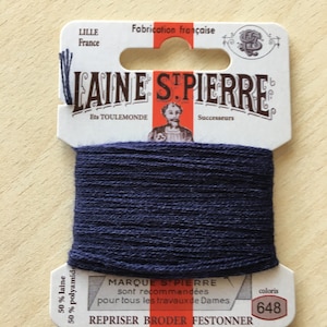 May include: A spool of dark blue embroidery thread with a white label that reads "LAINE STPIERRE" and "REPRISER BRODER FESTONNER". The label also indicates the thread is 50% wool and 50% polyamide. The color number is 648.