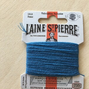 May include: A spool of blue embroidery floss with a white label that reads "LAINE STPIERRE Ets TOULEMONDE Successeurs MARQUE STPIERRE sont recommandées pour tous les travaux de Dames REPRISER BRODER FESTONNER coloris 735". The label also states "50% laine 50% polyamide" and "Fabrication française".