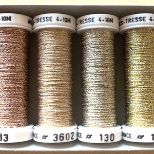 Op de afbeelding: Een doos met zes spoelen metallic garen in goud, zilver en ros&eacute; goud. De spoelen zijn genummerd: 002, 013, 3602, 130, 128 en 102.