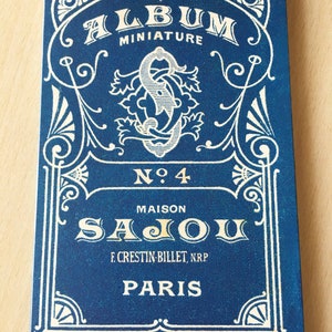 May include: A blue and white vintage-style label with the text "ALBUM MINIATURE N°4 MAISON SAJOU F. CRESTIN-BILLET, NRP PARIS".