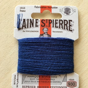 May include: A spool of dark blue yarn labeled "LAINE STPIERRE" with the text "50% laine 50% polyamide" and "coloris 930". The label also says "MARQUE STPIERRE sont recommandées pour tous les travaux de Dames" and "REPRISER BRODER FESTONNER".