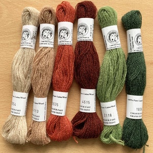 Peut inclure: Six écheveaux de fil de laine 100% pure dans différentes couleurs, dont beige, orange, marron, vert et vert foncé. Chaque écheveau porte une étiquette avec le nom de la marque "Laine Dauphinoise", le poids du fil et le numéro de la couleur.