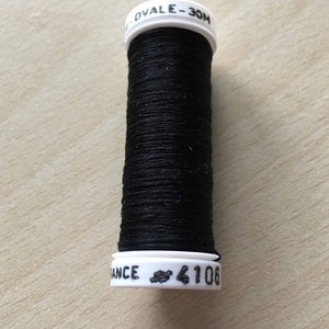 Puede incluir: Una bobina de hilo negro con etiquetas blancas que dicen "OVALE - 30M" y "ANCE # 4106".