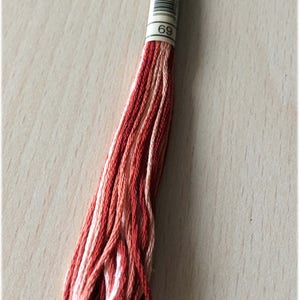 Pode incluir: Um novelo de fio para bordar em tons de vermelho, laranja e branco. O fio é etiquetado com o número "69".