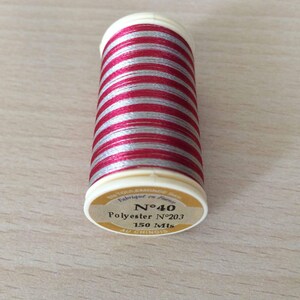 Può includere: Un'bobina di filo rosso e argento con un'etichetta che recita "N°40 Polyester N°203 150 Mts AU CHINOIS".
