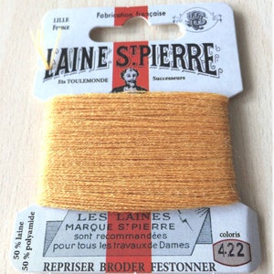 May include: A spool of Laine St. Pierre thread in color 4.22. The thread is a warm, golden-yellow color. The label reads "Laine St. Pierre" and "Fabrication française". The thread is 50% wool and 50% polyamide.