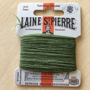 May include: A spool of green Laine St. Pierre thread, color 945, with a paper label. The label reads "Fabrication française" and includes text in French. The thread is recommended for various needlework projects.