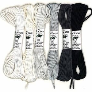 Puede incluir: Cuatro carretes de hilo de bordar en blanco, gris claro, gris oscuro y negro. Cada carrete está etiquetado con "Au fil a Soie d'Alger" y "100% Silk-Soie - Eta-Seda - Paris".