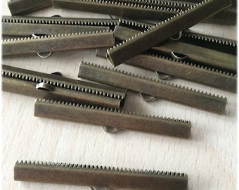 May include: A pile of 12 antique brass metal slider clasps, each with a serrated edge and a small loop on one end. The clasps are approximately 5 cm long.