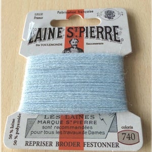 May include: A spool of light blue yarn labeled "LAINE STPIERRE" with the text "LES LAINES MARQUE STPIERRE sont recommandées pour tous les travaux de Dames REPRISER BRODER FESTONNER" and "coloris 740".