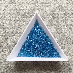 May include: A white triangular tray filled with a large pile of small, light blue iridescent glass beads.