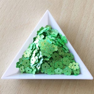 May include: A white triangular tray filled with green iridescent flower-shaped sequins.