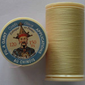 Peut inclure: Une bobine de fil beige clair avec une étiquette qui indique "FIL A GANT Coton Fabrique en France Glacé APPLICATIONS 120 150 m AU CHINOIS".