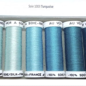 May include: Six spools of turquoise thread labeled "Soie 1003 Turquoise" with the text "A SOIE-1001 VER A SOLA SOIE-100 AU VER AU VER VER A SO" and "X-FRANCE SOIE/SILK-FRA BLK-FRANCE 100% SOIE/ 100% SOIE/ME/SILK-FRAK"