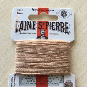 Peut inclure: Une bobine de fil à broder beige avec une étiquette blanche qui indique "LAINE STPIERRE" et "LES LAINES MARQUE STPIERRE sont recommandées pour tous les travaux de Dames REPRISER BRODER FESTONNER" avec le numéro de couleur "290".