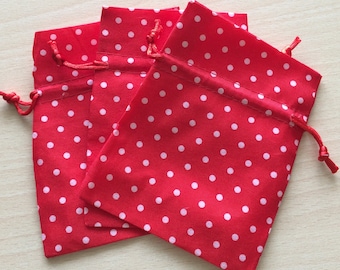 May include: Three red fabric gift bags with white polka dots. The bags have a drawstring closure.