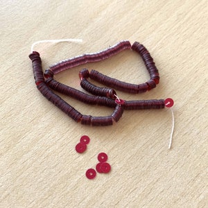 Peut inclure: Un brin de paillettes marrons enfilées sur un fil blanc, avec quelques paillettes détachées à proximité.