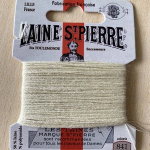 May include: A spool of beige embroidery thread labeled "Laine St Pierre" with the text "Les Laines Marque St Pierre sont recommandees pour tous les travaux de Dames" and "Repriser Broder Festonner". The spool is labeled with the color number "841".