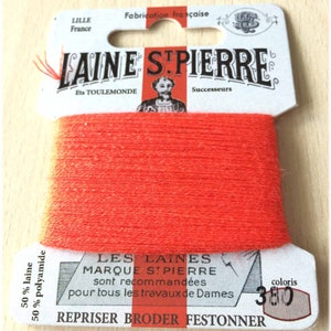 May include: A spool of orange embroidery floss labeled "LAINE ST PIERRE" with the text "LES LAINES MARQUE STPIERRE sont recommandées pour tous les travaux de Dames" and "REPRISER BRODER FESTONNER" on the label. The spool is labeled "coloris 380".