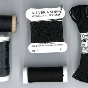 Puede incluir: Cuatro carretes de hilo negro, dos con carretes de madera y dos con carretes de plástico blanco. Un carrete está etiquetado con "AU VER A SOIE® METALLICS AU SEXTANT" y tiene una muestra del hilo adjunta. La etiqueta también dice "Fabriqué en France 35% poliéster, 65% Cupro Bemberg 10 m 4".