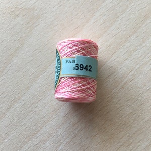 Può includere: Un'bobina di filo da ricamo rosa e bianco con un'etichetta blu che dice "NU CHINO FAB. 5942".