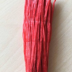 Peut inclure: Un paquet de raphia de papier rouge, un type de fibre naturelle utilisée pour l'artisanat et la décoration.