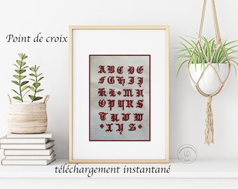 May include: A framed cross-stitch pattern of the alphabet in a gothic font. The letters are red on a white background. The frame is light wood and the text below the image reads "téléchargement instantané".