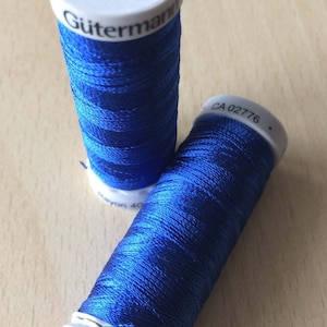 May include: Two spools of blue thread, one labelled "Gutermann" and "Swiss made" and the other labelled "100% Viscose".