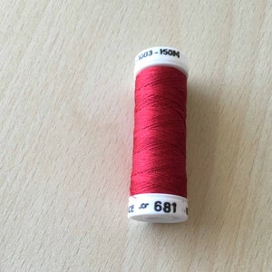 May include: A spool of red thread with white labels. The labels read "1003 - 150M" and "681".