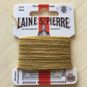 Peut inclure: Une bobine de fil à broder doré avec une étiquette blanche qui indique "LAINE STPIERRE Ets TOULEMONDE Successeurs" et "MARQUE ST PIERRE sont recommandées pour tous les travaux de Dames REPRISER BRODER FESTONNER" avec le numéro de couleur "368".