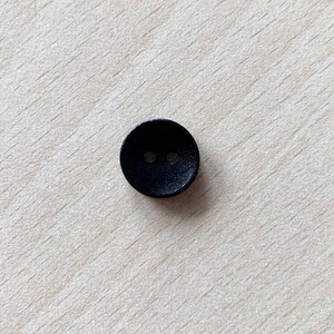 May include: A black button with two holes. The button is round and has a smooth surface.