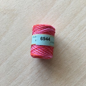 May include: A spool of pink and orange embroidery floss with a blue label that reads "FAB F 6944 J.T.O."