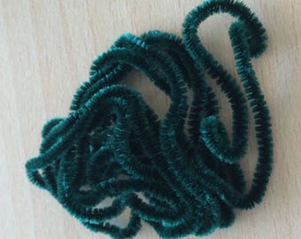 May include: A pile of dark green pipe cleaners, also known as chenille stems, are twisted and curled together.