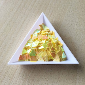 May include: A white triangular dish filled with iridescent yellow triangle-shaped sequins.