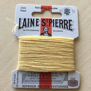 Könnte beinhalten: Eine Spule gelbes Laine St. Pierre-Garn, Farbe 318, mit einem Etikett mit der Aufschrift "Fabrication française". Das Etikett enthält auch den Text "REPRISER BRODER FESTONNER" und "LES LAINES MARQUE ST. PIERRE sont recommandées pour tous les travaux de Dames."