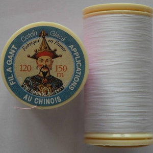 May include: A spool of white thread with a pink label. The label says "Fil a Gant Coton Fabrique en France Glacé Applications Au Chinois" and features a man in a traditional Chinese robe. The spool is 120 metres long.