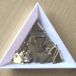 May include: A white triangular tray filled with silver triangle-shaped metal embellishments.
