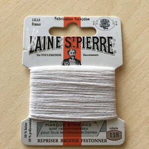 May include: A spool of white embroidery thread with a label that reads "LAINE STPIERRE" and "MARQUE STPIERRE sont recommandées pour tous les travaux de Dames". The label also includes the text "REPRISER BRODER FESTONNER" and the color number "118".