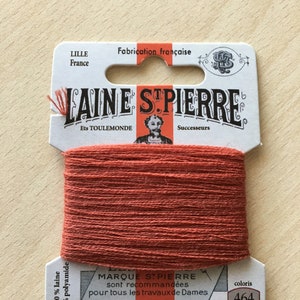 Op de afbeelding: Een spoel rode borduurgaren met het label "LAINE STPIERRE" en de tekst "50% laine 50% polyamide" en "coloris 464".