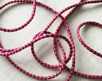 May include: A close-up of a red and gold braided cord. The cord is made of a soft, silky material and has a subtle sheen.