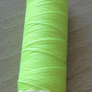 Może przedstawiać: Szpulka jasnożółtej nici z białą etykietą z napisem "100 m" i "yester".