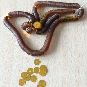May include: A strand of brown sequins with a pile of gold sequins scattered on a wooden surface.